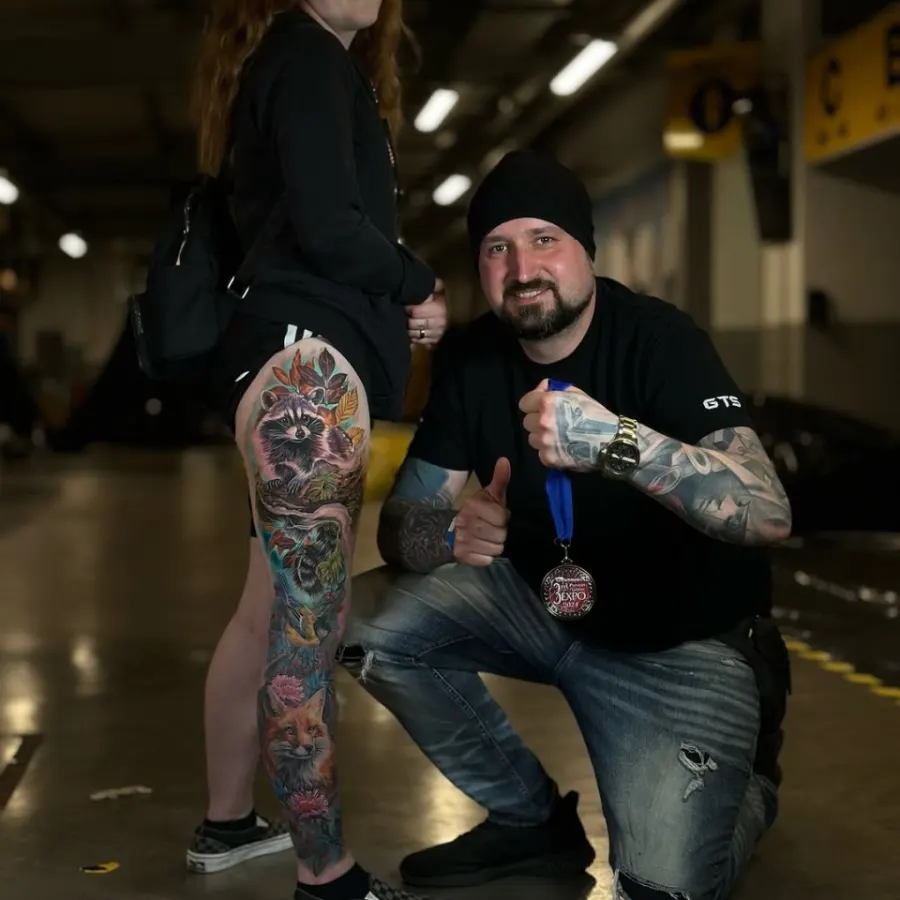 Vitālijs ar 3. vietas medaļu Preston Tattoo Expo 2024 blakus klientei ar jenota kājas piedurkni