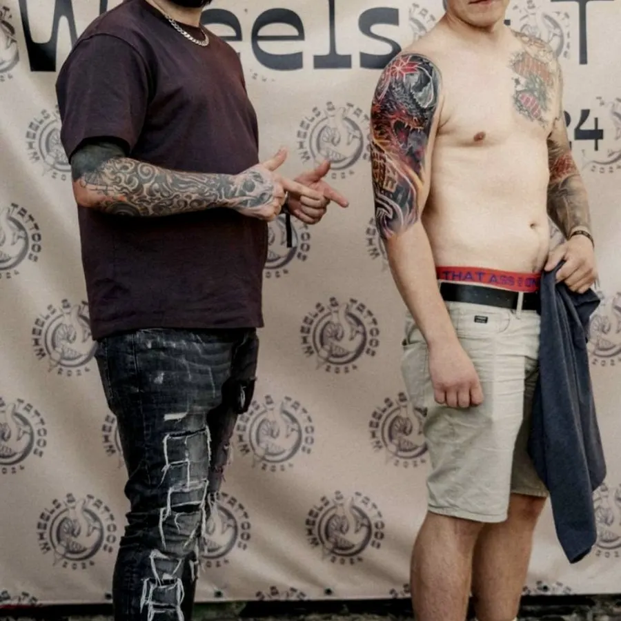Vitālijs festivālā Wheels and Tattoos 2024 ar klientu un krāsainu pūķa piedurkni